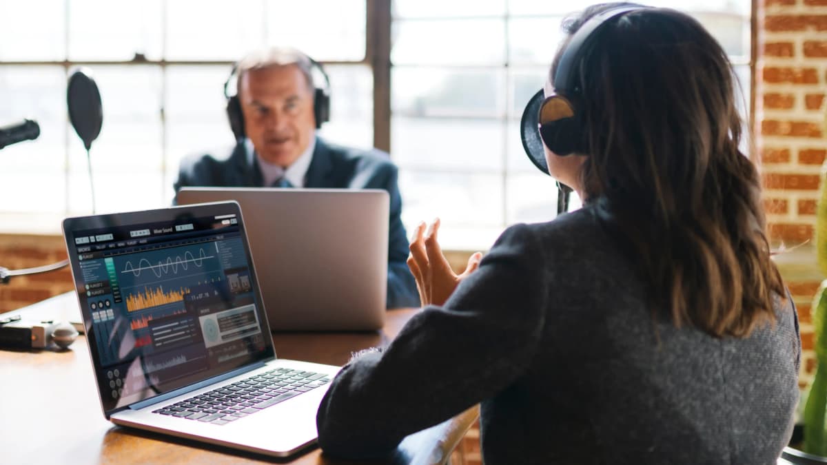 Female podcast host talking to male attorney, both wearing headphones.