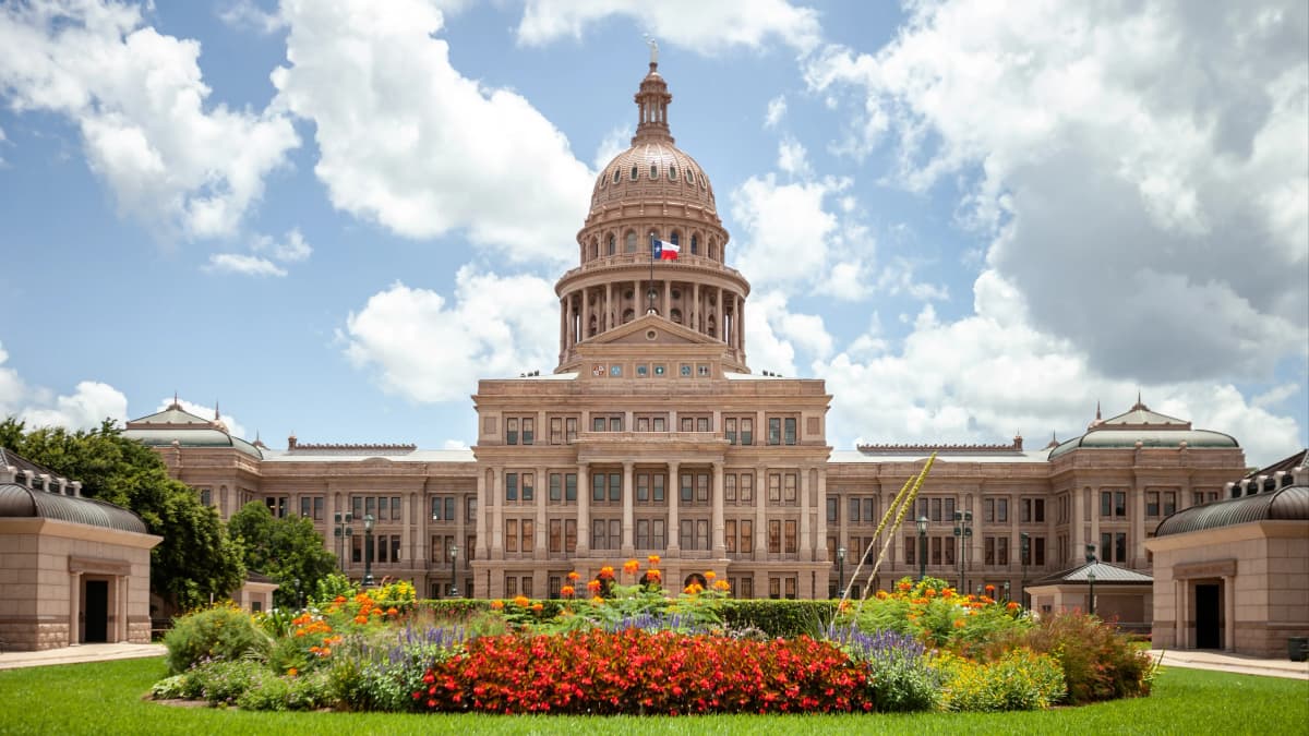 Texas State Capitol building in Austin, Texas on sunny day with clouds overhead.